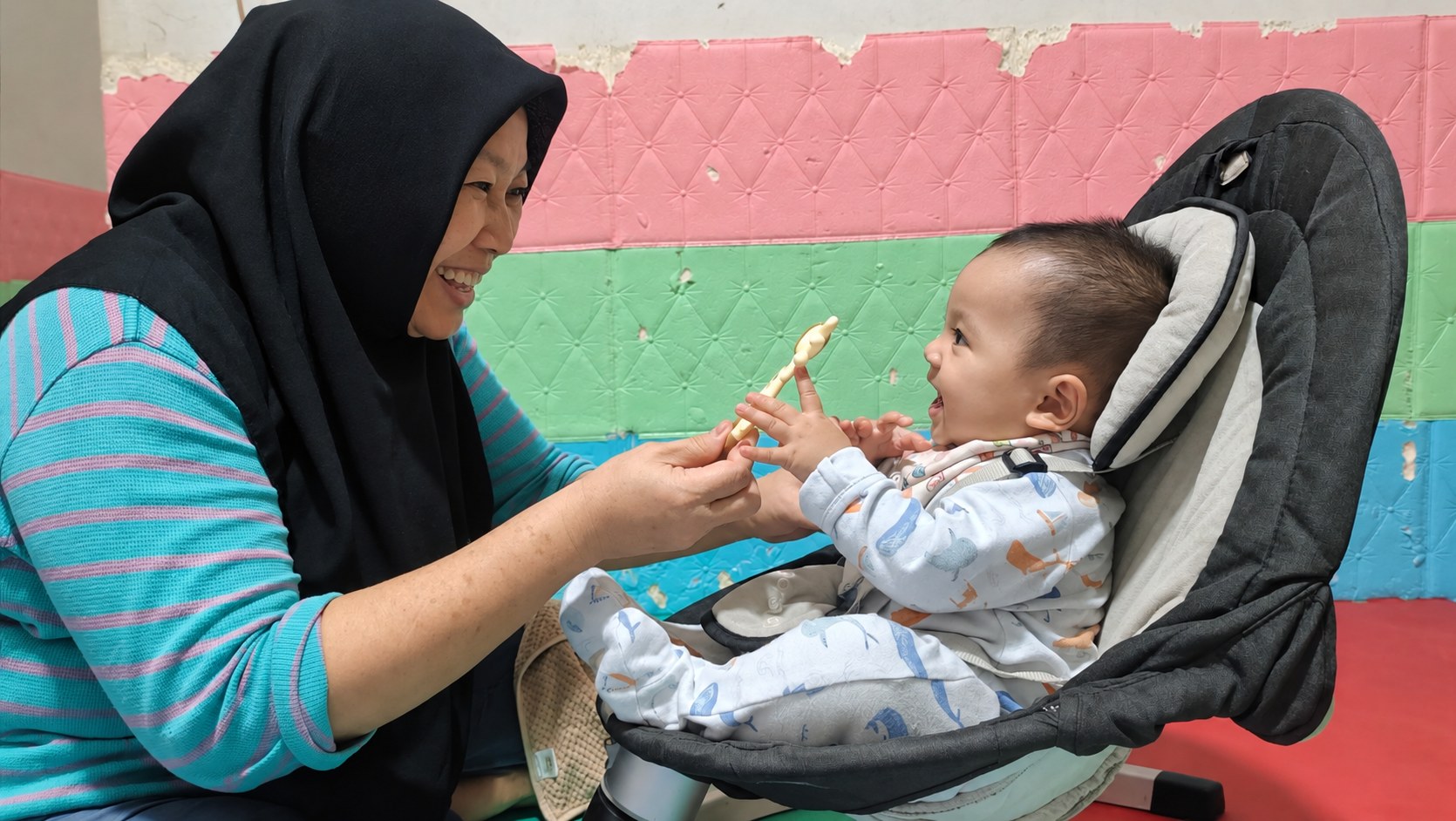 Pengasuh tersenyum dan bermain bersama bayi di Okaeri